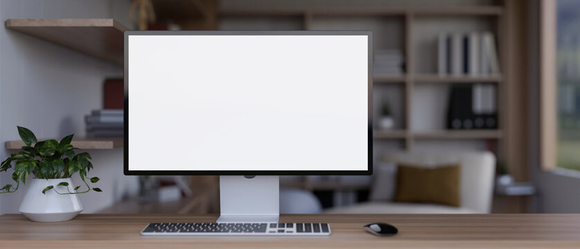 Front view image of a white-screen computer mockup on a wooden table in a modern living room.