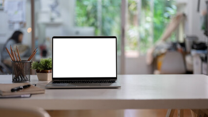 A white-screen laptop computer mockup and accessories on a white desk in a modern office.
