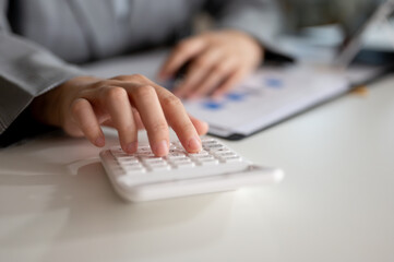 Close-up image of a professional Asian businesswoman using a calculator at a table in her office.