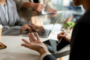 A businessman is taking notes on his tablet while having a meeting with his team in the office.