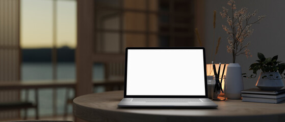 A white-screen laptop computer on a table in a modern dark room.