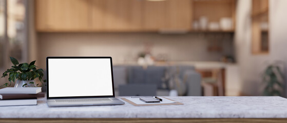 A white-screen laptop computer and stationery on a white marble table in a modern living room.