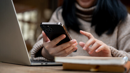 An Asian woman using her smartphone, responding to messages while sitting at a table in a cafe.
