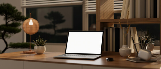 A laptop computer mockup and accessories on a wooden table in a modern, cosy working room at night.