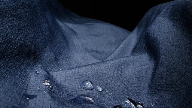 Waterproof clothing for tourism. Blue cloth texture with water drop close-up macro. Repellent waterproof breathable fabrics. Innovation waterproofing material test