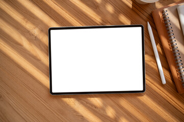 Top view image of a digital tablet mockup on a wooden table with a tablet pen and stationery.