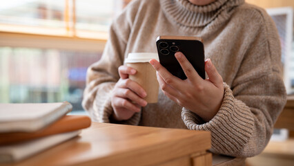 Cropped shot of a woman is using her smartphone and enjoying her morning coffee in a coffee shop.