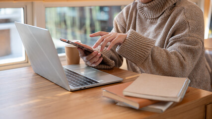 Cropped shot of a woman is checking messages on her phone while working remotely at a cafe.