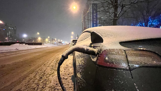 Moscow 26 January 2024, Electric car at night on city charging in snowdrifts. Tesla electric car charging in winter at night