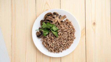 Buckwheat porridge with boiled mushrooms, willow herbs on wooden background