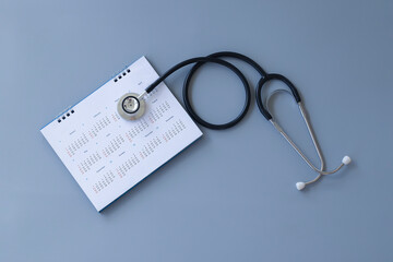 Black stethoscope and calendar on gray background, health concept	
