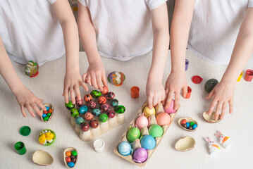 Obraz na płótnie Canvas Children's hands take painted Easter eggs from the table. On the table are Easter eggs, chocolate eggs and candy, Easter decorative decorations. Religious holiday concept