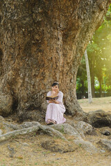 Woman seated next to a tree trunk in a park reading a book. World book day. Concept of reading.