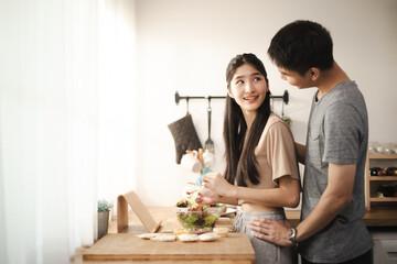 Happy couple Asian standing in kitchen at home preparing together yummy lunch on first dating,...