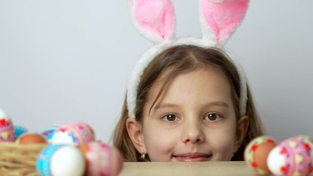 Easter egg hunt. Cute girl with bunny ears behind the table with eggs