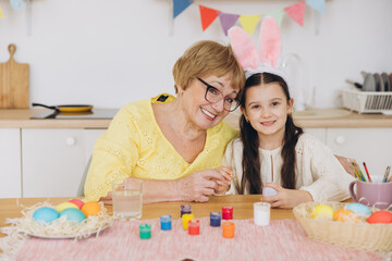 Obraz na płótnie Canvas Happy easter! A grandmother and her granddaughter painting colorful eggs