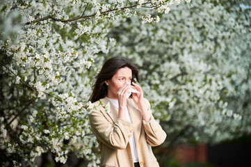 Woman allergic suffering from seasonal allergy at spring in blossoming garden at springtime. Young...