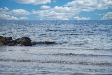 Fototapeta premium By the sea of the Baltic Sea. Stone groynes reach into the blue water. White clouds in the sky. Landscape shot of the coast.