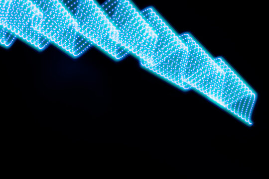 Blue neon curved wave of light as curls or swirl with dotted stripes on black background. Abstract background with motion light effect, light painting in holiday style.