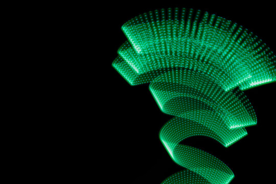 Turquoise green neon curved wave of light as funnel or swirl with dotted stripes on black background. Abstract background with motion light effect, light painting in festive style.
