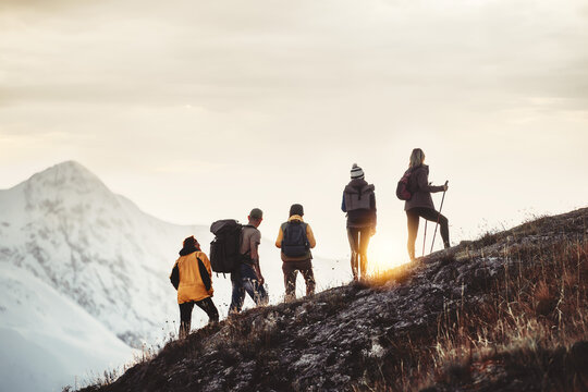 Group of mixed age hikers are standing on mountain slope and looking at sunset