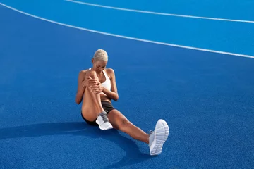 Fototapeten An African American female athlete engages in warm-up exercises, sitting on the Olympic blue track, embodying the concept of race training and dedication in sports © amedeoemaja