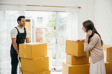 Professional movers aid couple indoors unloading boxes from truck into the home. Service guarantees...