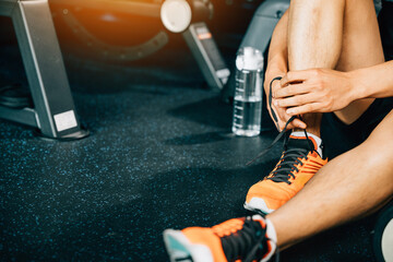 Young Asian man tying his shoelaces in his home gym before starting his workout routine. The shot showcases his sporty shoes and the water bottle he uses to stay hydrated during exercise