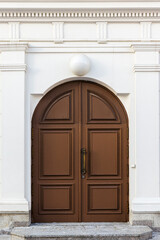 Brown wooden arched door in white wall, classic architecture background