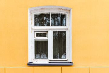 Arched window with white wooden frame in yellow wall