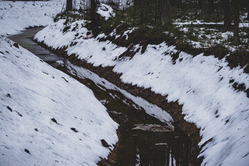 Fresh clean drainage ditch covered with snow in winter forest. Water running at bottom