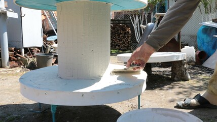 a craftsman creates handmade products by applying a layer of mastic to a piece of furniture with a cylindrical base and a round tabletop, coating a table made with his own hands with plaster