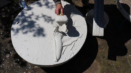 applying a layer of mastic with a spatula to the surface of a round piece of furniture outdoors on a sunny day, the work of a craftsman to create original products using construction materials