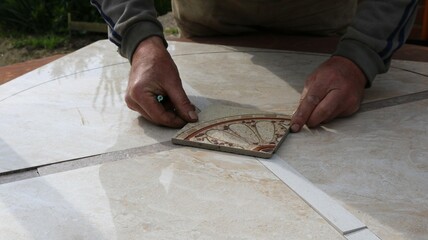 male hands lay out a square tile with a pattern in the middle of a mosaic made from large parts of...