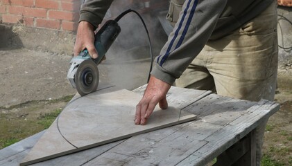 a master saws off a large piece of tile along the circumference using a miter saw in an outdoor workshop, cutting out a round shape of ceramic material with a circular saw on the street