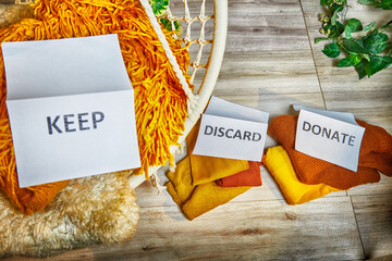 Signs with the words keep, donate, discard and fashion clothes folded in stacks in cozy room. The...