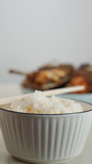 White rice in a bowl and fried fish on a white plate are served on the table