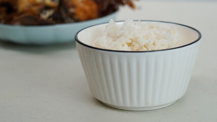 White rice in a bowl and fried fish on a white plate are served on the table