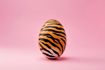 Zelfklevend Fotobehang A unique egg adorned with vivid tiger stripes on a simple pink background exemplifies artistic surrealism © Glittering Humanity