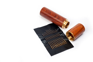 Metal sewing needles for hand sewing on a faux leather base and a container for storing them.
