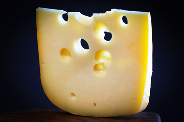 Slice of Emmental on cutting board on black background