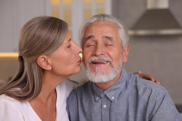 Senior woman kissing her beloved man in kitchen