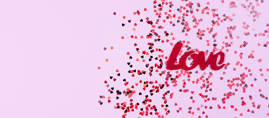 A word LOVE and small red hearts on the pink background. Composition for Valentine's Day. Flatlay. Banner. Top view. Copy space. Selective focus.