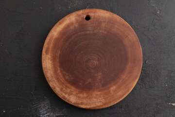 Empty round wooden cutting board on black concrete. Top view