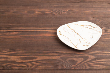 Empty white and gold ceramic plate on brown wooden. Side view, copy space