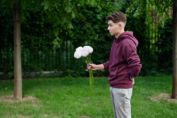 A young man stands with flowers and looks into space. He handed flowers to his friend, but she left