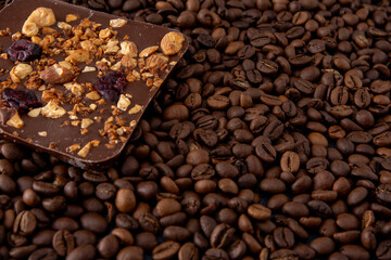 A bar of craft chocolate with various nuts, berries and dried fruits. Coffee beans. Food brown background