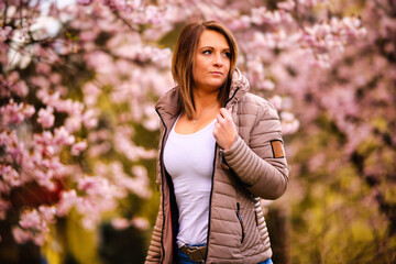 A young woman stands in a sea of ​​cherry blossoms and smiles into the camera. Cherry blossoms on the tree in full pink bloom.