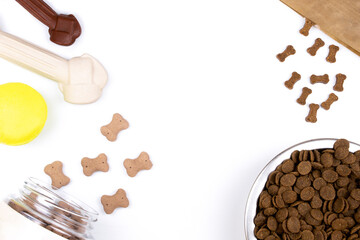 Top view of dog food: dry food in metal bowl, bone-shaped treats and cookies, tennis ball on a white background. Dog food concept