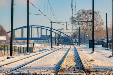 Electric cables on snow covered train tracks, provincial railway station and bridge in foggy...